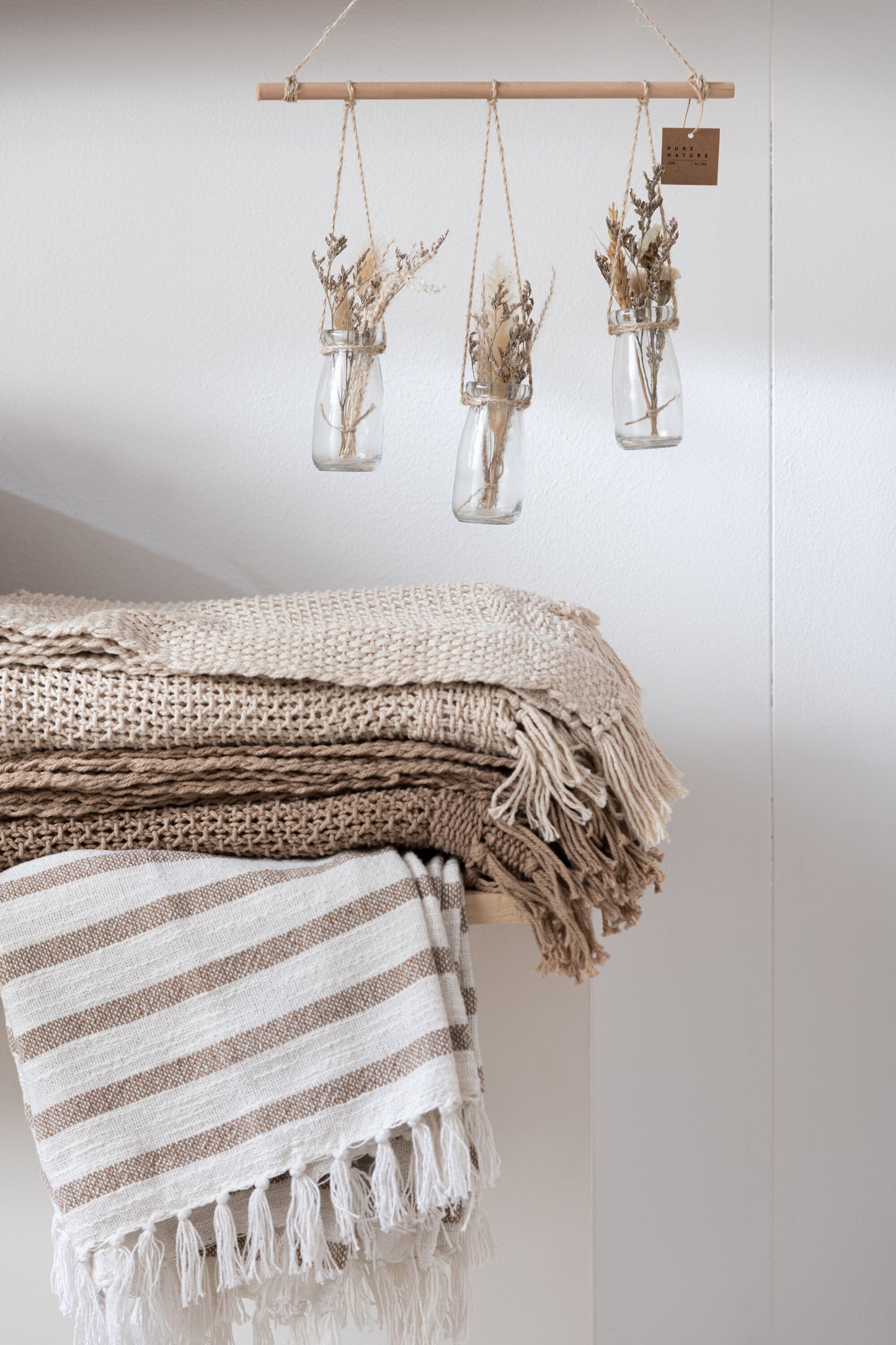 Neutrale woondecoratie met beige plaids en wandhanger met glazen vaasjes en droogbloemen