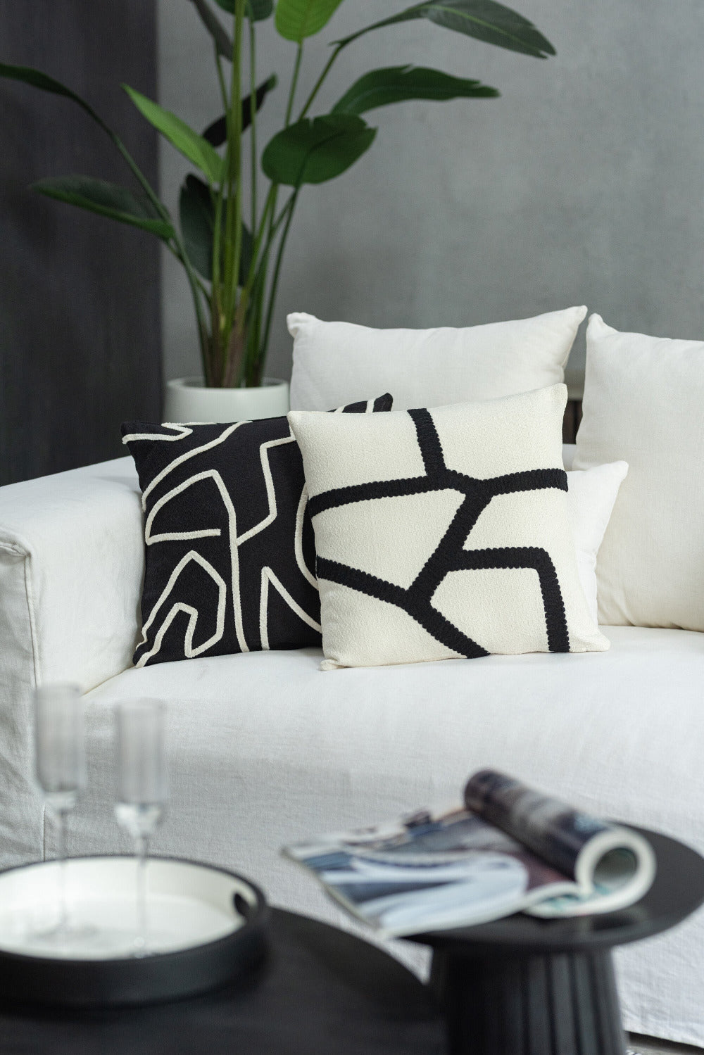 Moderne witte sofa met zwart-witte sierkussens in grafisch patroon, minimalistisch interieur met groene kamerplant en zwart bijzettafeltje