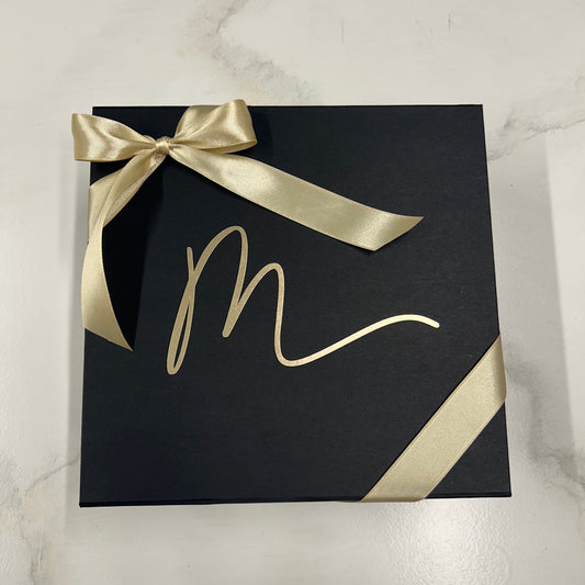 Gesloten zwarte Mari-Ve geschenkdoos met gouden lint. – luxe cadeauverpakking met gouden linkt en M-logo van Mari-Ve