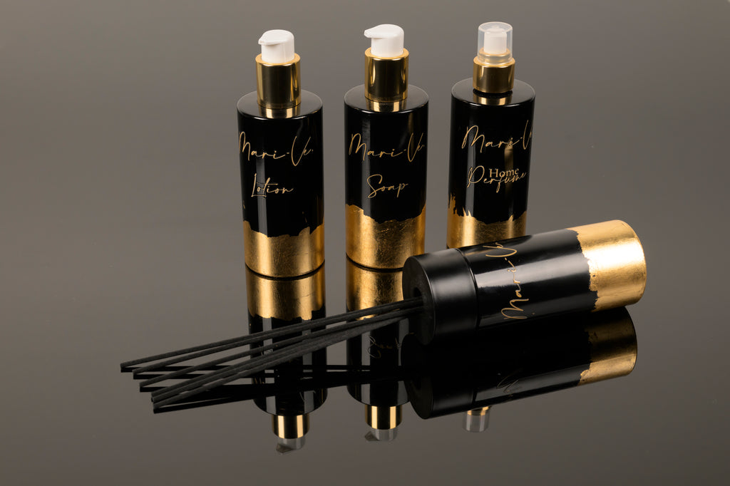 Mari-Ve® Luxe collectie met lotion, zeep, roomspray en diffuser in elegante zwart-gouden flacons, stijlvol gepresenteerd op een glanzend zwarte ondergrond.
