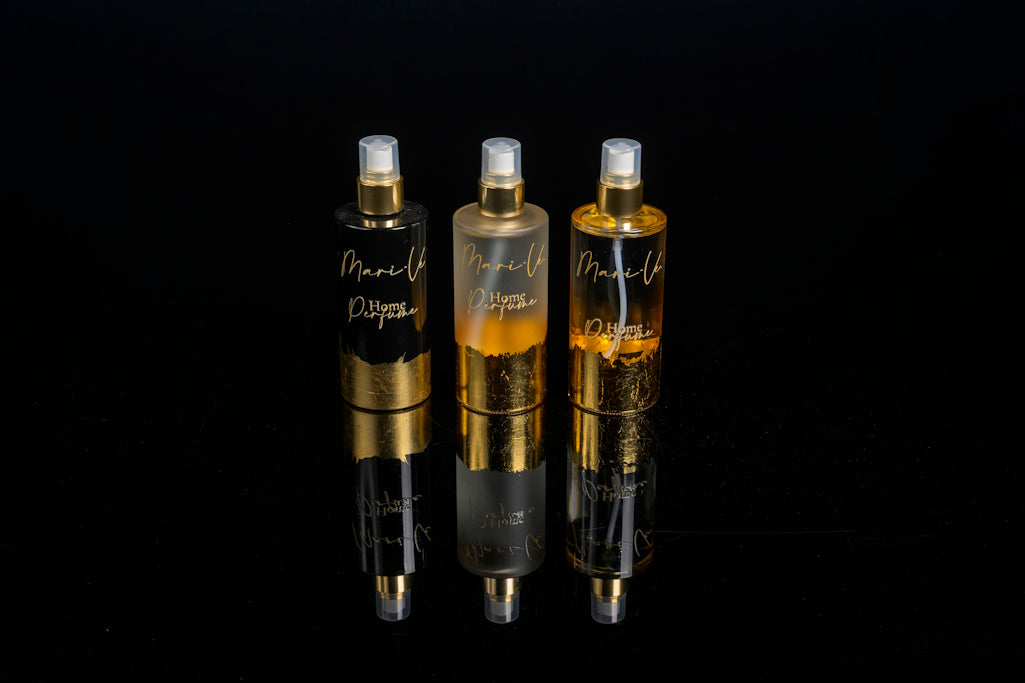 Drie exclusieve home perfumes uit de Mari-Ve collectie, gepresenteerd in elegante flacons met gouden accenten en luxe uitstraling, gefotografeerd tegen een glanzende zwarte achtergrond.